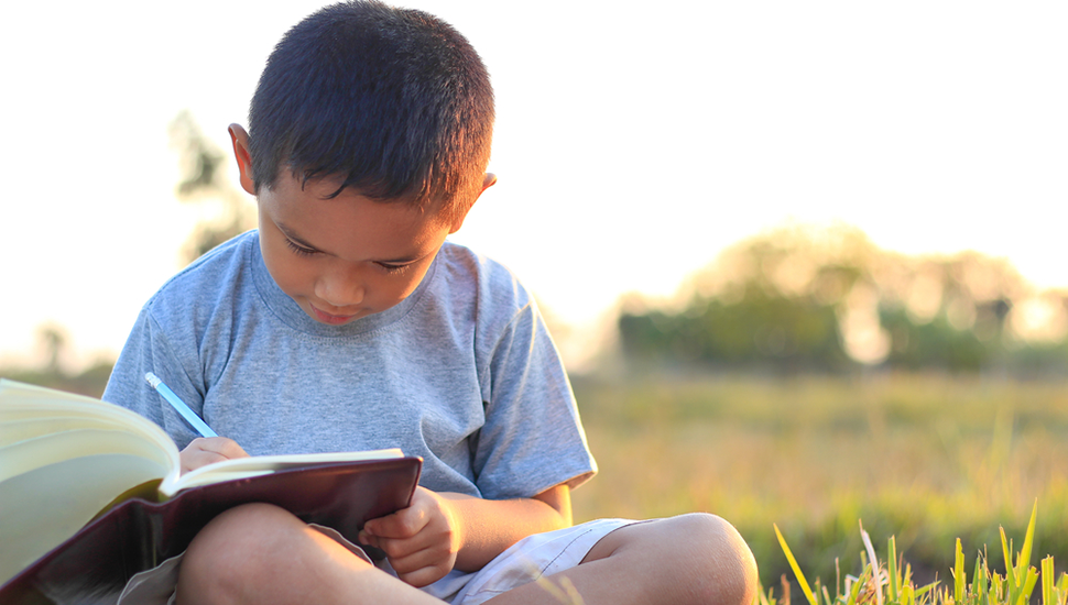A young boy reading a book outside