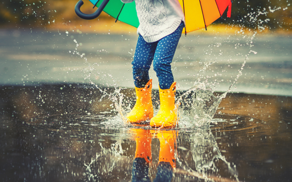 A young child holding an umbrella jumps in a rain puddle.