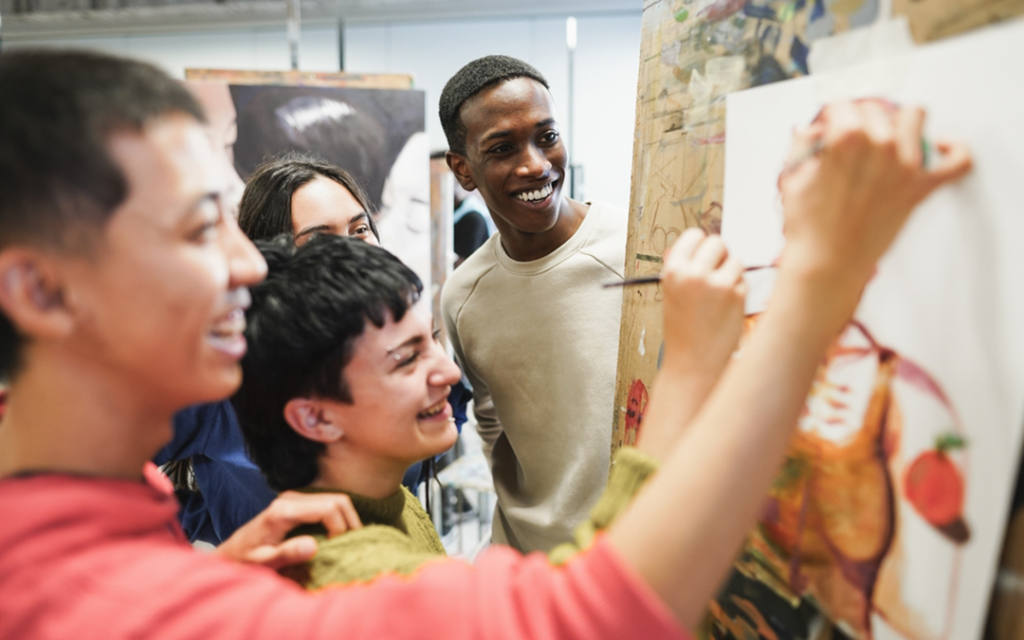 Diverse group of teens laugh while working together on an art project