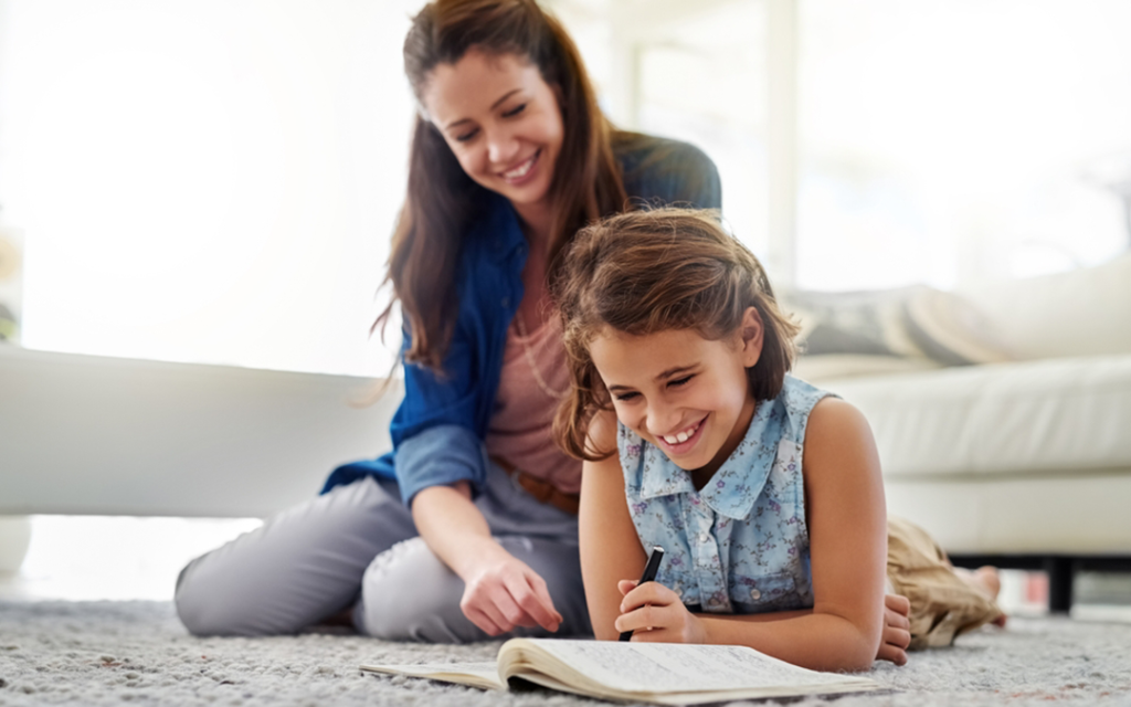 Mom and preteen daughter sit on the floor reading from notebook the floor