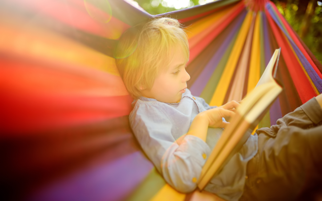 Young boy sits in a hammock reading a book