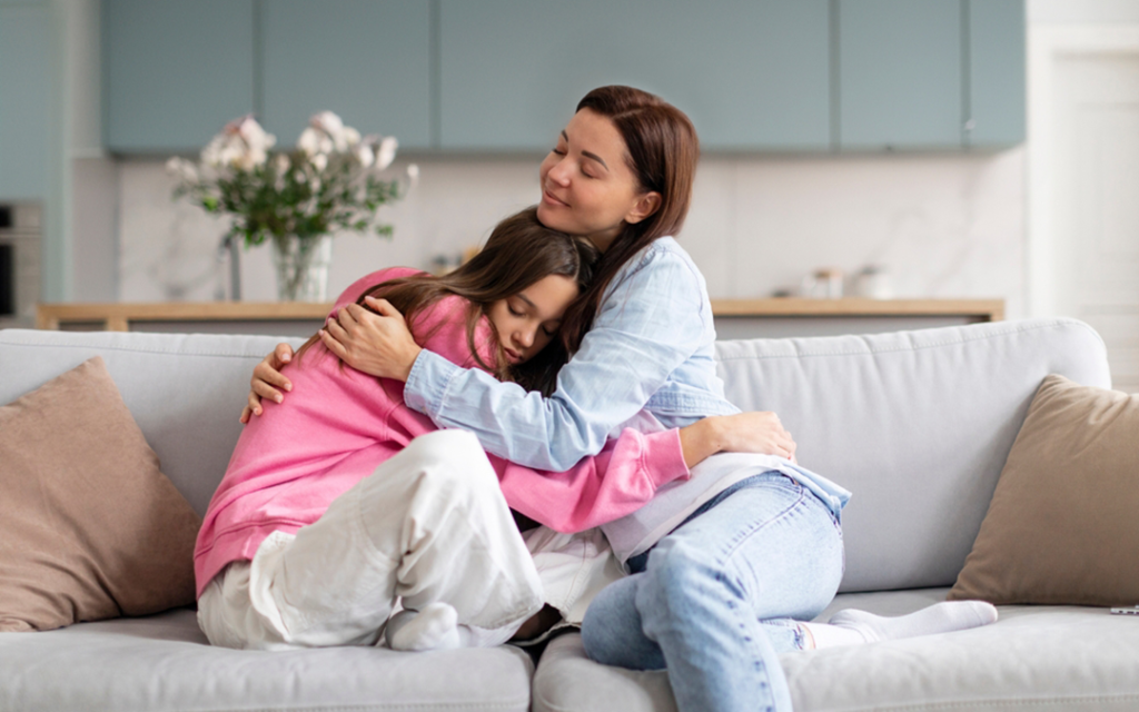 Mother hugs and comforts teenage daughter on the couch