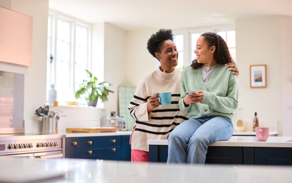 Mother and teen daughter talk and laugh together in kitchen