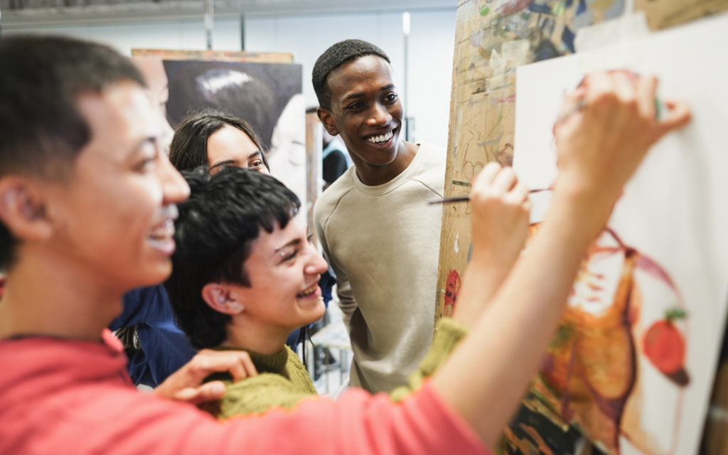 A group of 4 students painting on a canvas together.