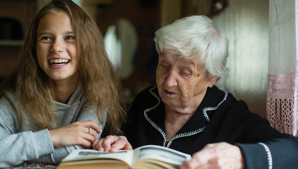 Teen girl and grandmother read a book together.