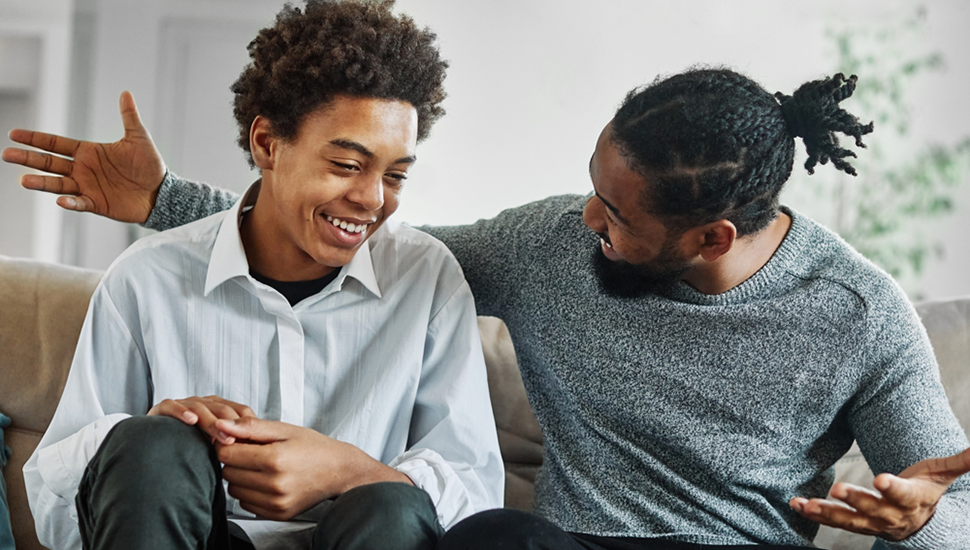 Father and son sit on the couch having a discussion, laughing.