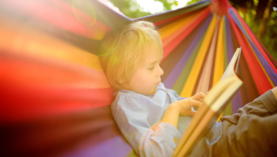 Young boy sits in a hammock reading a book
