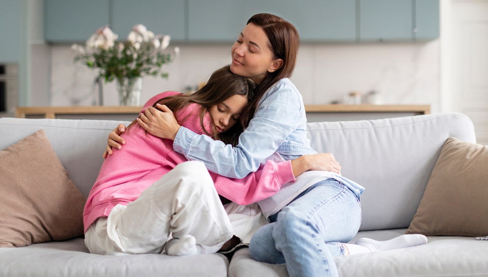 Mother hugs and comforts teenage daughter on the couch