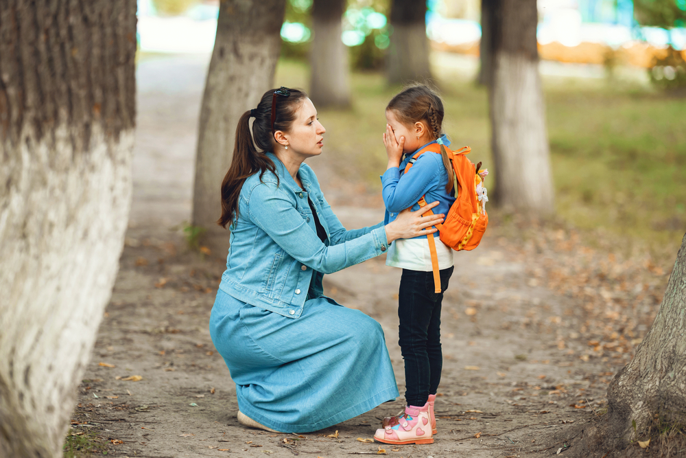 The adult is kneeling down, comforting a crying child