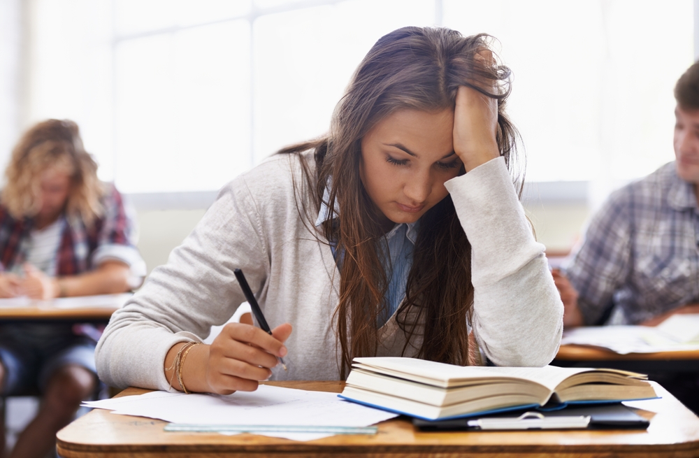 A teenage girl, sitting at a desk, stressed about her schoolwork.