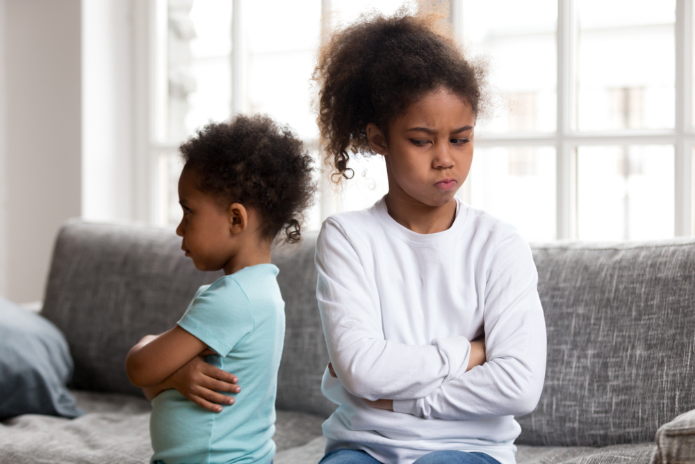 Two siblings, a young boy and girl, are facing away from each other angry.