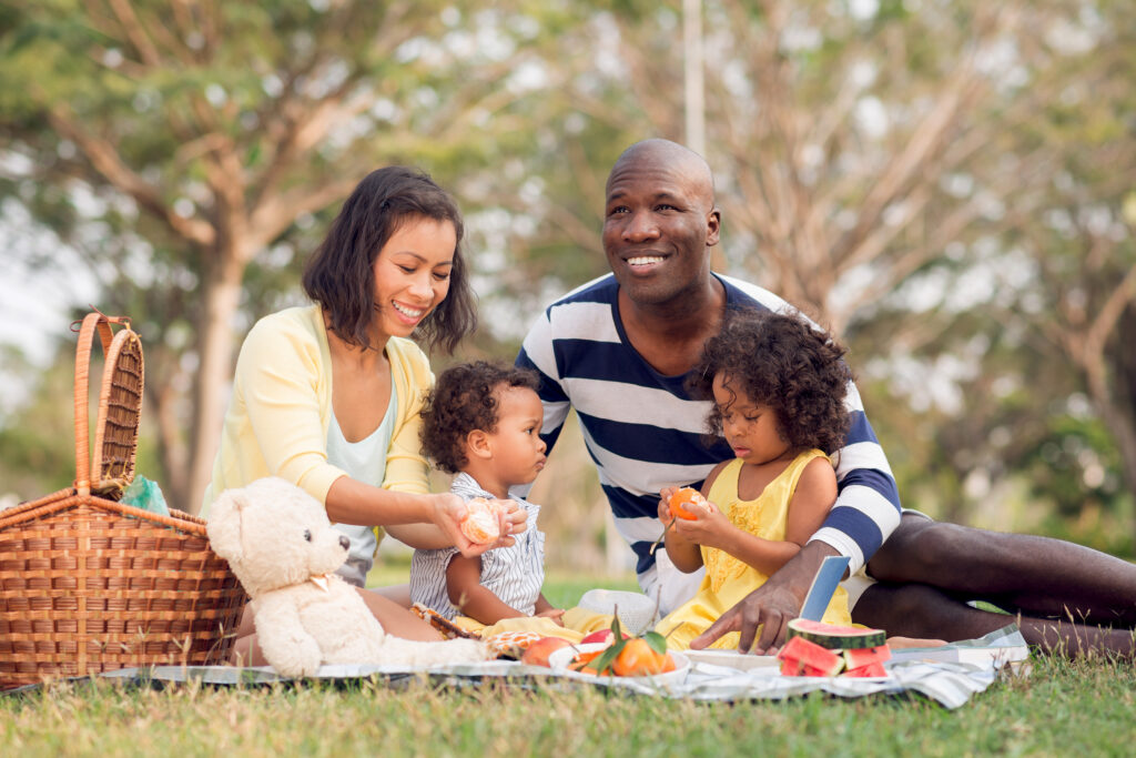 A family of four, sitting in the grass, having a picnic outside.