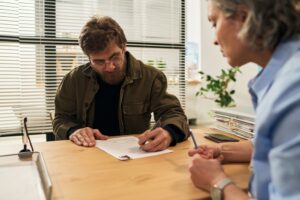 Middle,Aged,Caucasian,Man,Sitting,At,Desk,Signing,Paperwork,With