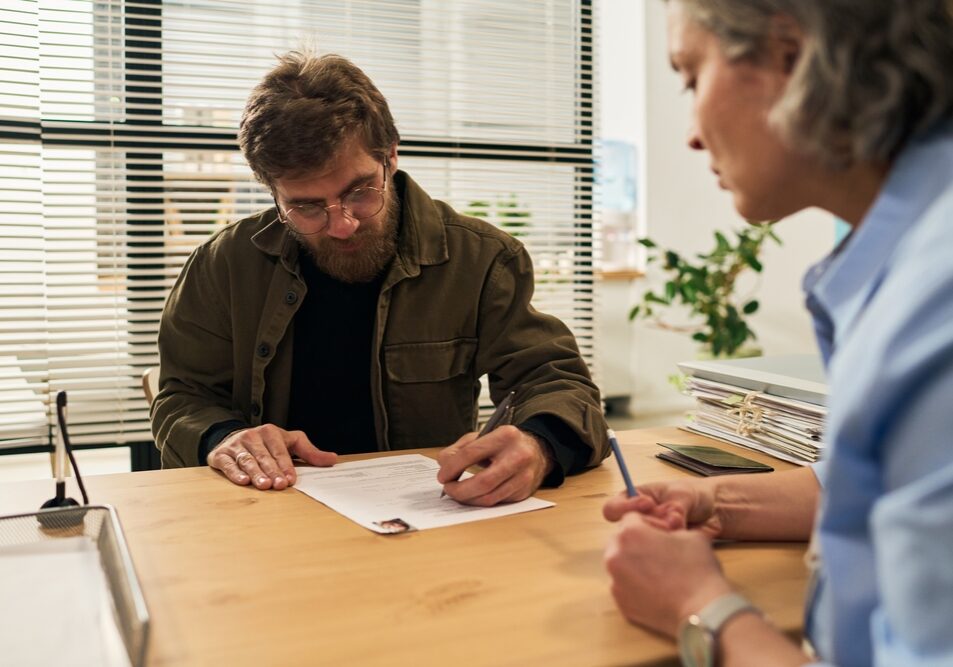 Middle,Aged,Caucasian,Man,Sitting,At,Desk,Signing,Paperwork,With